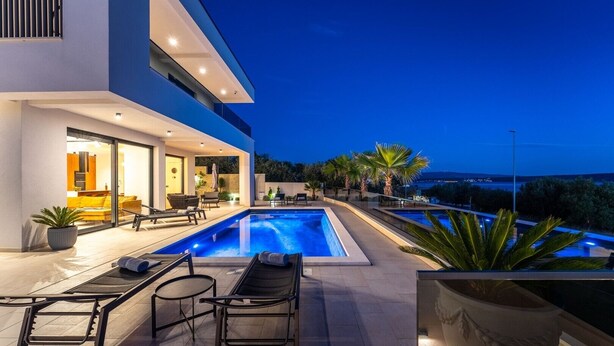 A modern outdoor pool area with a clear view of the sea, a covered seating area, and a well-lit entrance. - Luxury Villa Spectrum pool 32m2 sauna, family, sea view, bbq (Posedarje)