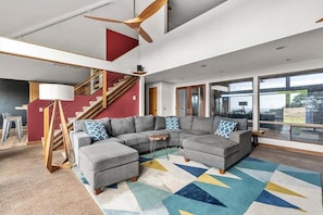 A modern living room with a sectional sofa, a ceiling fan, and a staircase. - Moorings | Ocean Views | Hot Tub | Dog Friendly (The Sea Ranch)