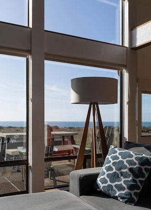 A room with a large window, a floor lamp, and a sofa with a patterned pillow. - Moorings | Ocean Views | Hot Tub | Dog Friendly (The Sea Ranch)