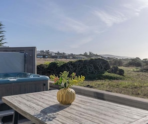A hot tub on a wooden deck with a view of a grassy field and distant buildings. - Moorings | Ocean Views | Hot Tub | Dog Friendly (The Sea Ranch)