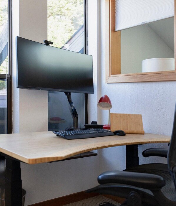 A modern office desk with a computer monitor, keyboard, and a red desk lamp. - Moorings | Ocean Views | Hot Tub | Dog Friendly (The Sea Ranch)