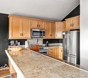 A kitchen with wooden cabinets, a stainless steel refrigerator, a microwave, and a granite countertop. - Moorings | Ocean Views | Hot Tub | Dog Friendly (The Sea Ranch)