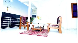 A room with a ceiling fan, a table with a floral centerpiece, and two wooden chairs. - Virat Home Stay (Nivari)