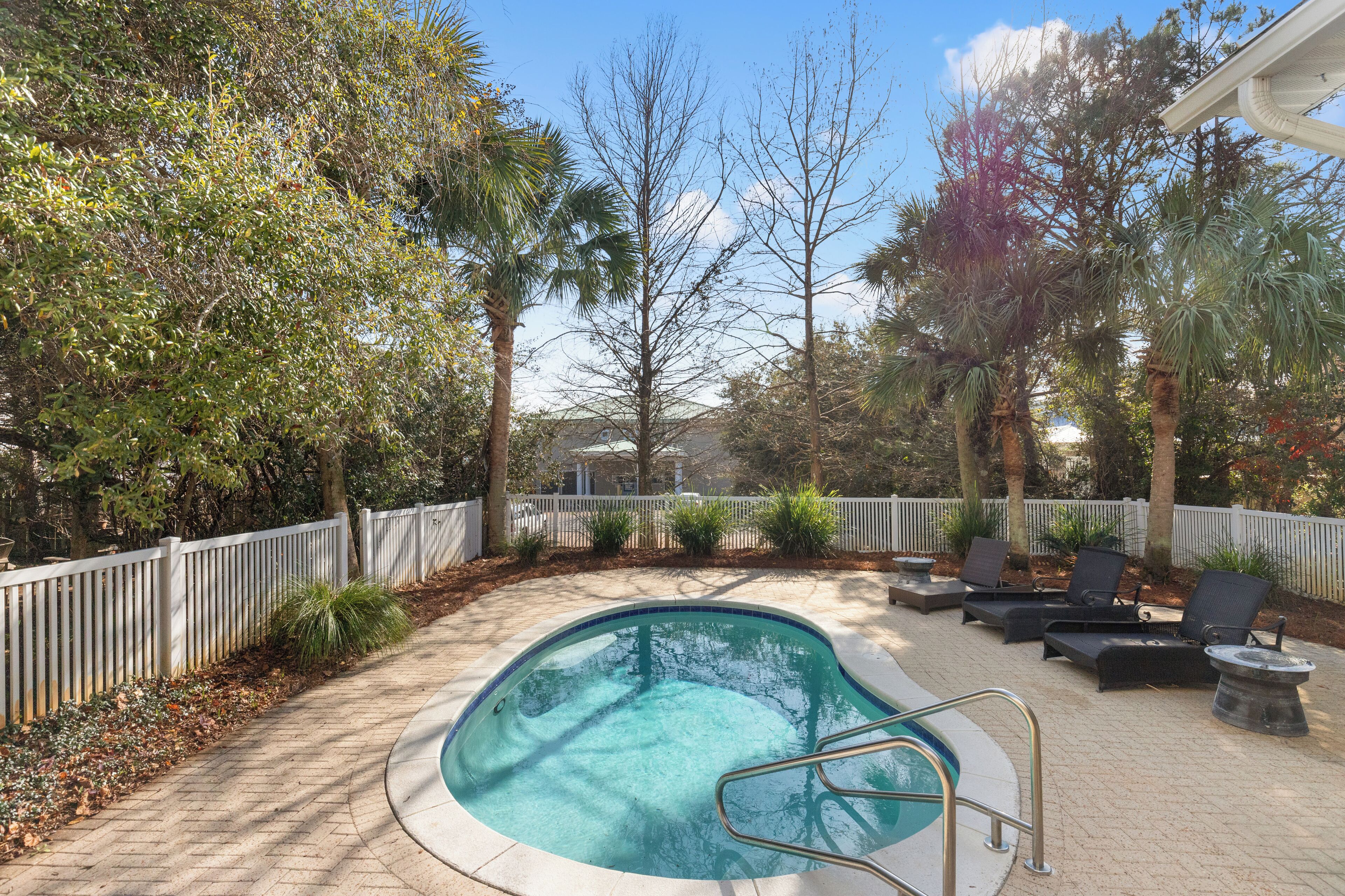 A swimming pool with lounge chairs and a white fence surrounding it.