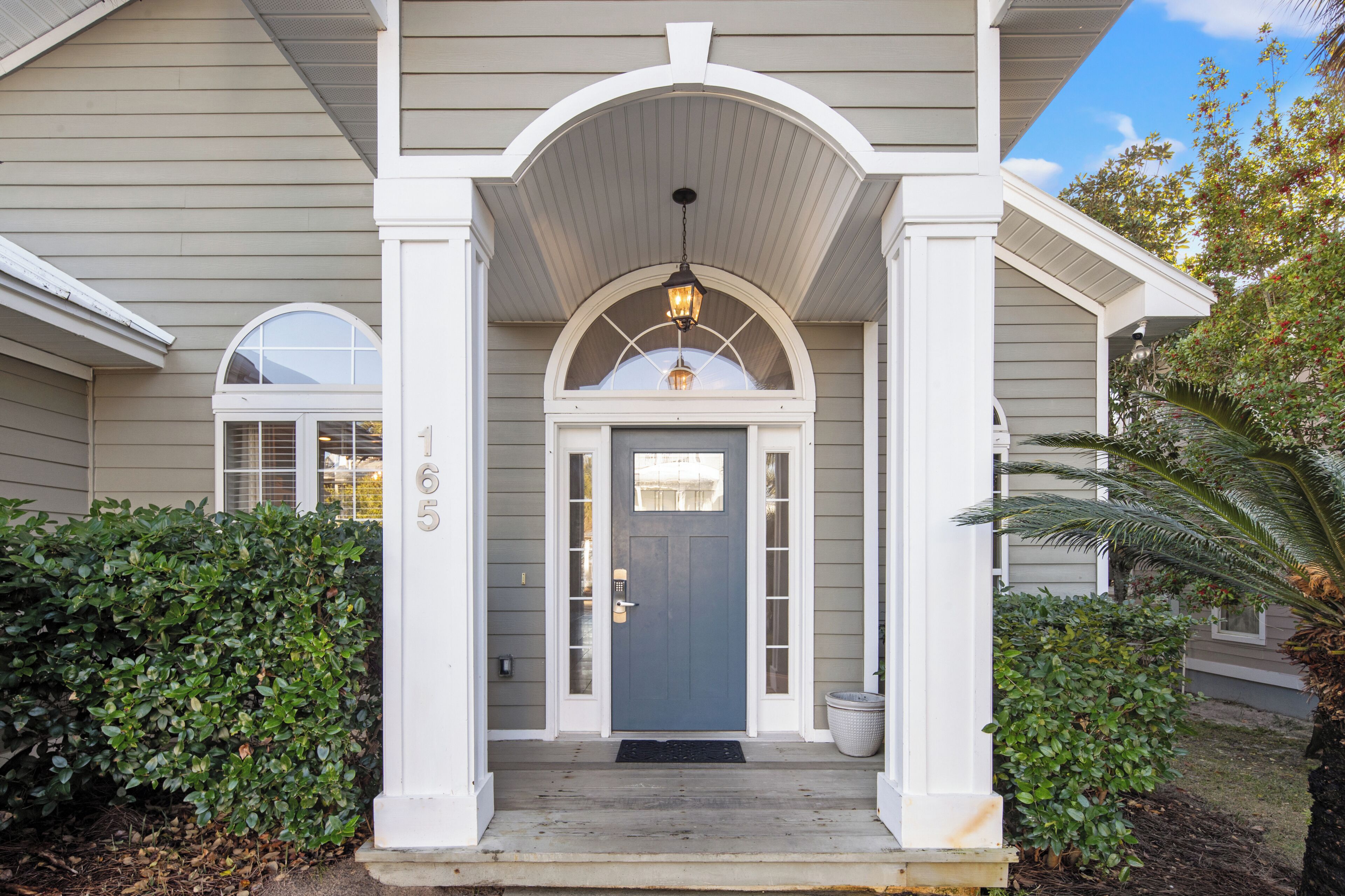 A house with a grey door, white columns, and a porch with a light fixture.