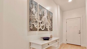A hallway with a white console table, a bowl, and three abstract paintings on the wall. - Book Now for Fall! Short Walk to Beach! Hot Tub! (Panama City Beach)