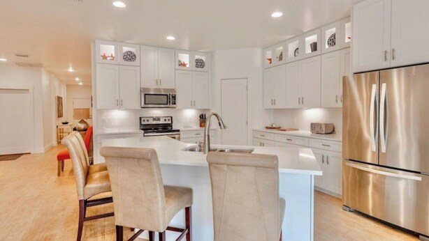 A modern kitchen with white cabinetry, stainless steel appliances, and a central island with bar stools. - Book Now for Fall! Short Walk to Beach! Hot Tub! (Panama City Beach)
