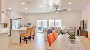 A modern kitchen with white cabinets, a central island, and a dining area with orange chairs. - Book Now for Fall! Short Walk to Beach! Hot Tub! (Panama City Beach)
