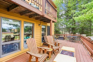 Una terraza de madera con sillas Adirondack y una mesa, con vistas a un área boscosa.