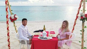 A beachside dining setup with a red tablecloth, white chairs, and a bottle of wine. - HI HEAVEN MALDIVES (Thoddoo)