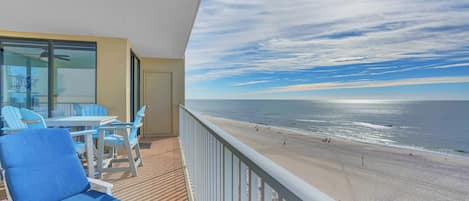 A balcony with a view of the beach, a table with chairs, and a ceiling fan.