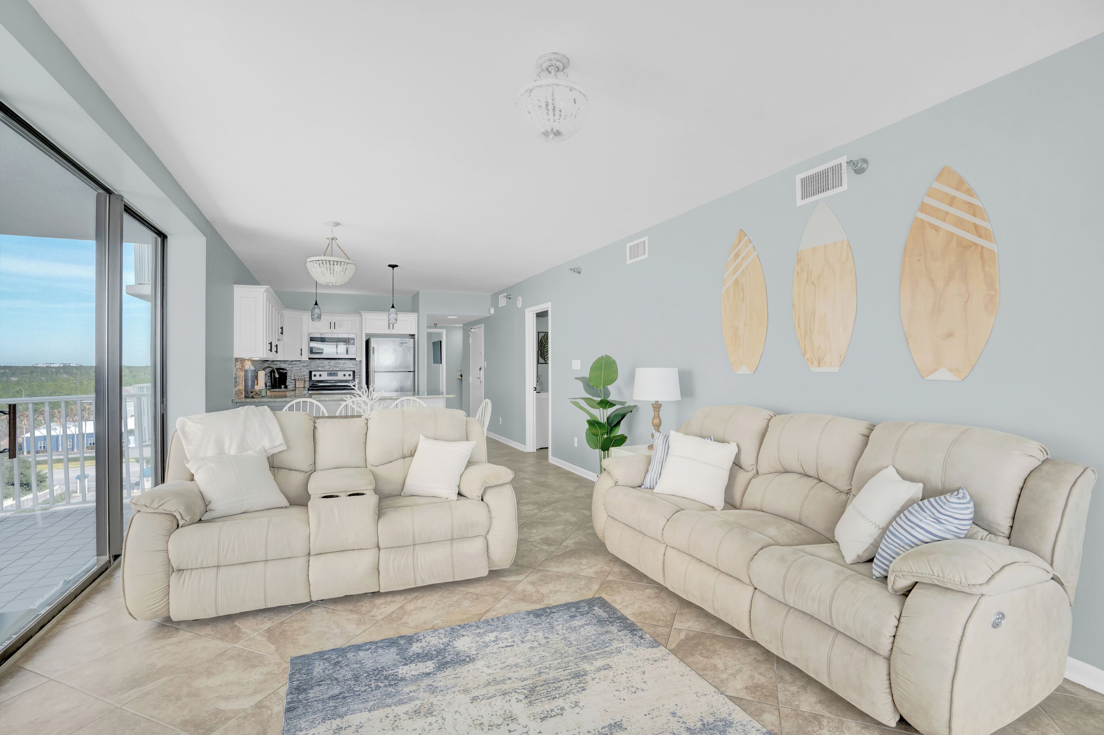 A spacious living room with two beige sofas, a coffee table, and a view of the kitchen and balcony.