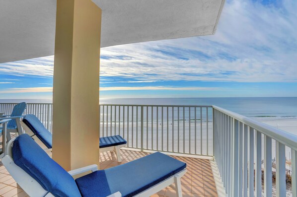 Balcón con dos sillones y una mesa, con vista a una playa y una barandilla.