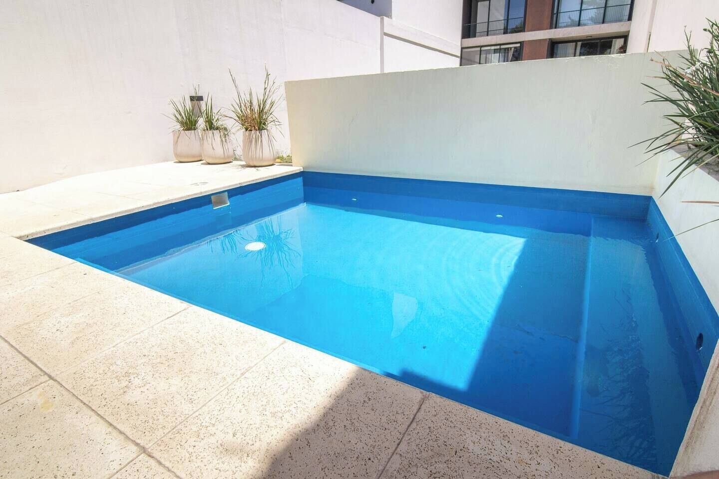 Une piscine rectangulaire aux parois bleues, entourée d’une terrasse carrelée de couleur claire.