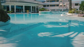 Une piscine aux eaux cristallines, équipée d’une bouée de sauvetage, entourée d’un bâtiment doté de nombreux balcons et d’un palmier.