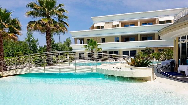 Ein Resort mit großem Pool, Palmen und einem mehrstöckigen Gebäude mit Balkonen.