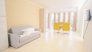 Una habitación de hotel moderna con un sofá gris, una mesita pequeña y sillas amarillas.