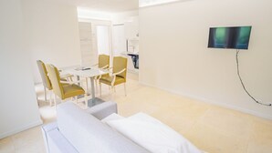 A modern hotel room with a dining area, a sofa, and a flat-screen TV mounted on the wall.