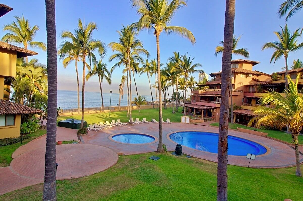 A resort with a pool area, palm trees, and a view of the ocean.