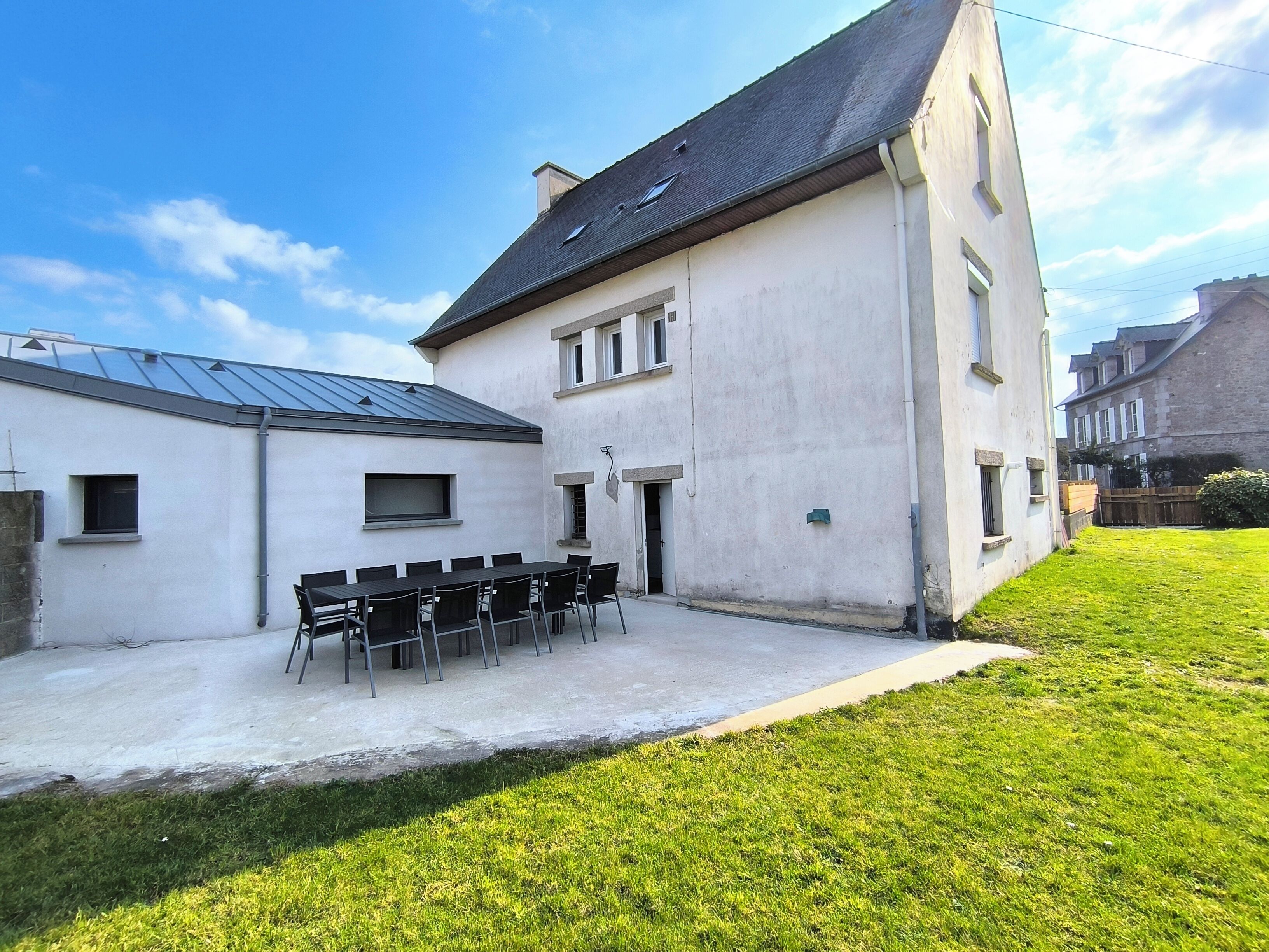 Een gebouw met een plat dak, een terras met een tafel en stoelen, en een verzorgd gazon.