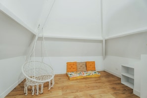 A room with a hanging chair, a sofa with cushions, and a wooden floor.