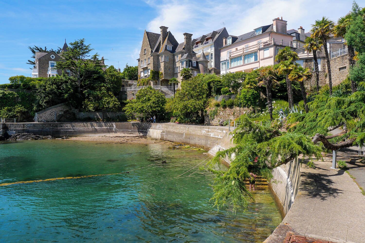 A coastal building with a stone facade, a clear view of the water, and a stone retaining wall.