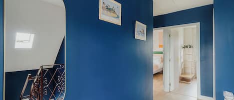 A hallway with blue walls, a large mirror, and two framed pictures.