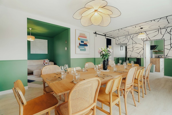 A dining area with a long wooden table set for six, surrounded by wicker chairs.