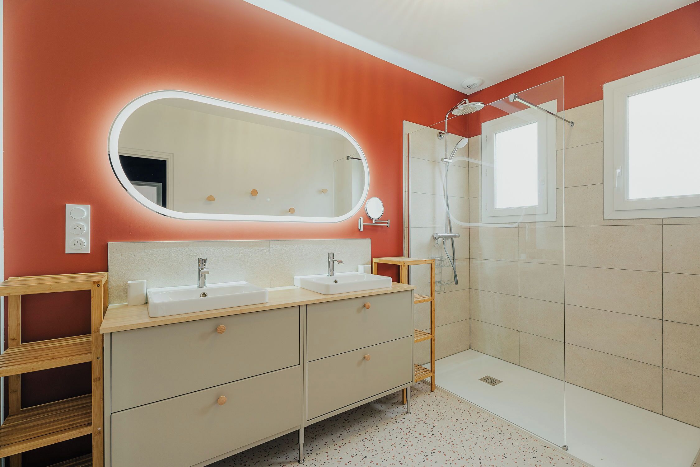 Une salle de bain avec deux lavabos, un miroir, une douche et une étagère en bois.