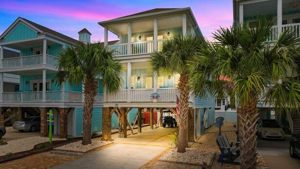 A multi-story hotel with a balcony on the second floor, palm trees in the courtyard, and a covered area with a vehicle parked inside. - Spacious 5BR/5.5BA Beach Home | Private Pool | 120 Steps to Beach | Near Pier (Surfside Beach)