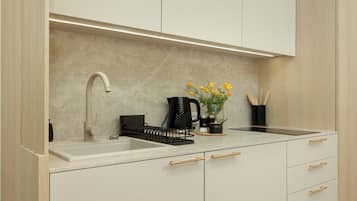 A modern kitchen with a white countertop, a black coffee maker, and a vase with yellow flowers.
