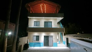 Edifici de dues plantes amb un balcó al pis superior, una escala que hi mena i una petita zona d'estar exterior amb una taula i caires.