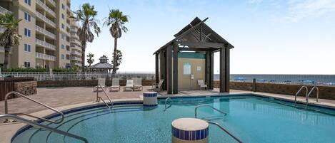A swimming pool with a wooden gazebo, lounge chairs, and a tall building in the background.