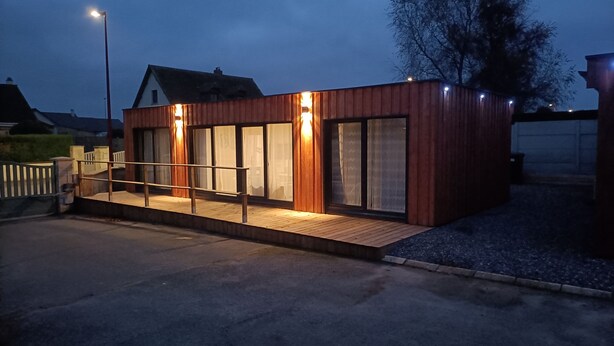 En moderne bygning med facade i træ, store vinduer og en træterrasse.