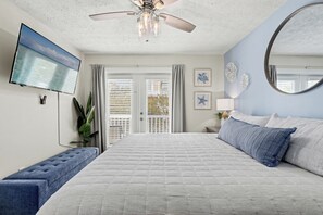 A bedroom with a large bed, a ceiling fan, a TV, and a balcony with curtains. - Escape to Sand Dollar Holler: Coastal Retreat, 3 Beds, 2.5 Baths, Sleeps 10! (Panama City Beach)