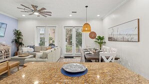 A modern kitchen with granite countertops, a dining area with white chairs, and a ceiling fan. - Escape to Sand Dollar Holler: Coastal Retreat, 3 Beds, 2.5 Baths, Sleeps 10! (Panama City Beach)