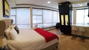 Habitación de hotel moderna con una cama grande, un escritorio y vistas a la ciudad a través de amplias ventanas.