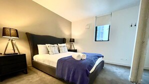 Ein Schlafzimmer mit einem Bett, zwei Nachttischen, einer Lampe, einem Fenster und einer Tür.