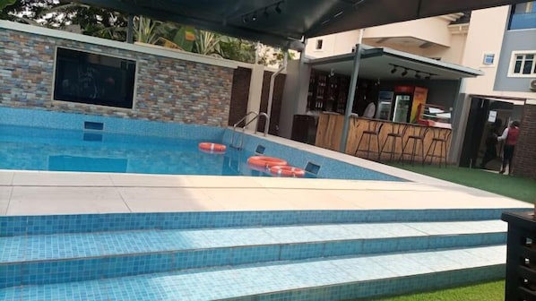 A swimming pool with steps leading into it, surrounded by a covered patio area with a bar and seating. - The Autograph Hotels and Apartments (Owerri)
