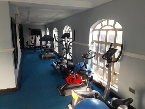 A gym with exercise equipment, a blue carpet, and large windows. - The Autograph Hotels and Apartments (Owerri)