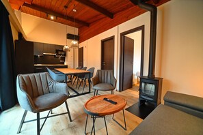 A modern living room with a sofa, chairs, a coffee table, a TV, a fireplace, and a kitchen in the background. - Chalet in Belgium With Stunning Views (Viroinval)