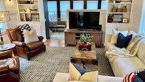 A living room with a leather armchair, a sofa, a coffee table with a vase, a television, and a bookshelf. - A Step Away: The Retreat – Walk to Town Escape (Saugatuck)