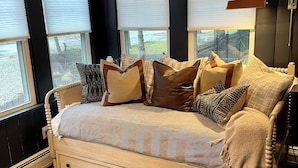 A bedroom with a bed, a bedside table, a lamp, and a window with blinds. - A Step Away: The Retreat – Walk to Town Escape (Saugatuck)