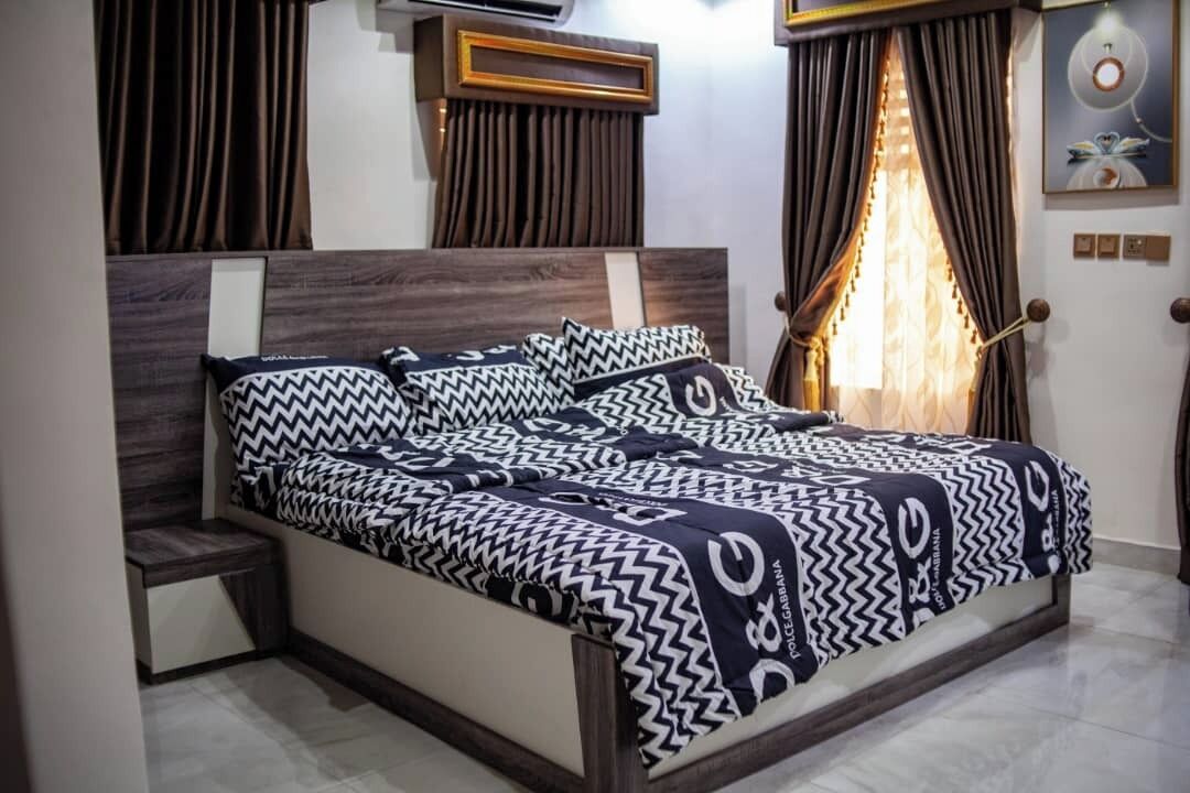 A neatly made bed with patterned bedding, a wooden headboard, and a bedside table.