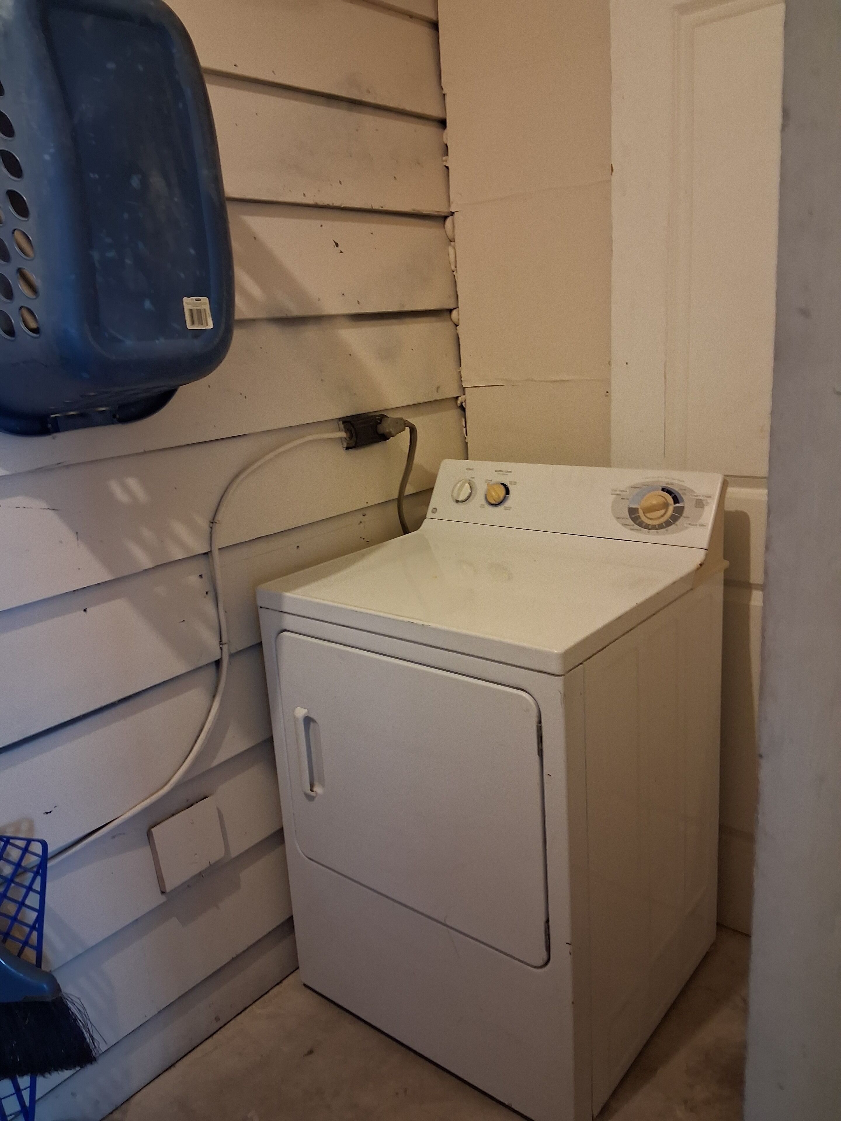 A compact white washer and dryer unit with a control panel on top, a blue laundry basket on the wall, and a door to the right.