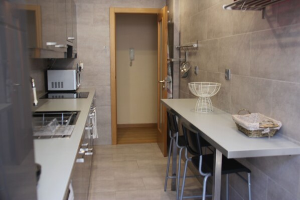 Une cuisine moderne avec un plan de travail blanc, des appareils en acier inoxydable et une porte en bois.