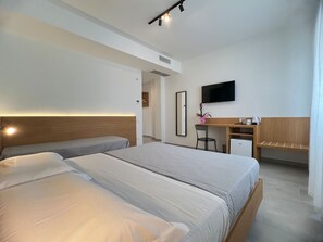 A modern hotel room with a large bed, a desk, a chair, a TV, and a small refrigerator. - Le camere del centro (Matera)