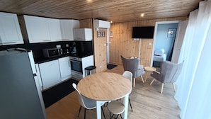 A compact kitchen with white cabinets, a microwave, and a coffee maker. There is a dining area with a round wooden table and two chairs. - Le Chalet Léna  (Petit-Caux)