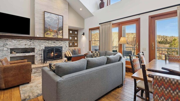Un salón espacioso con chimenea, un sofá grande color gris y una zona de comedor con sillas de madera.