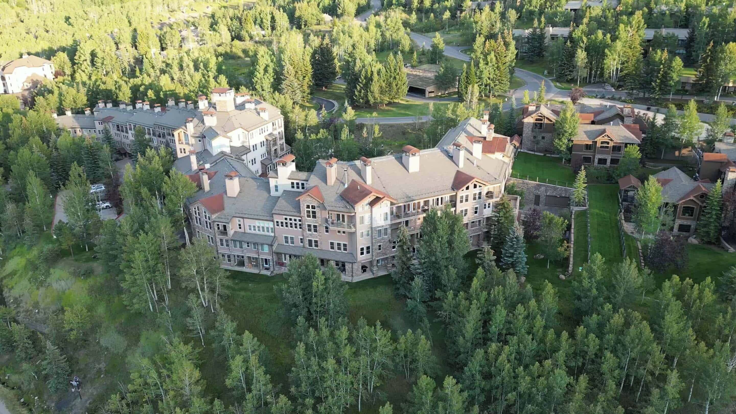 A large, multi-story building surrounded by dense forest, likely a resort or hotel.